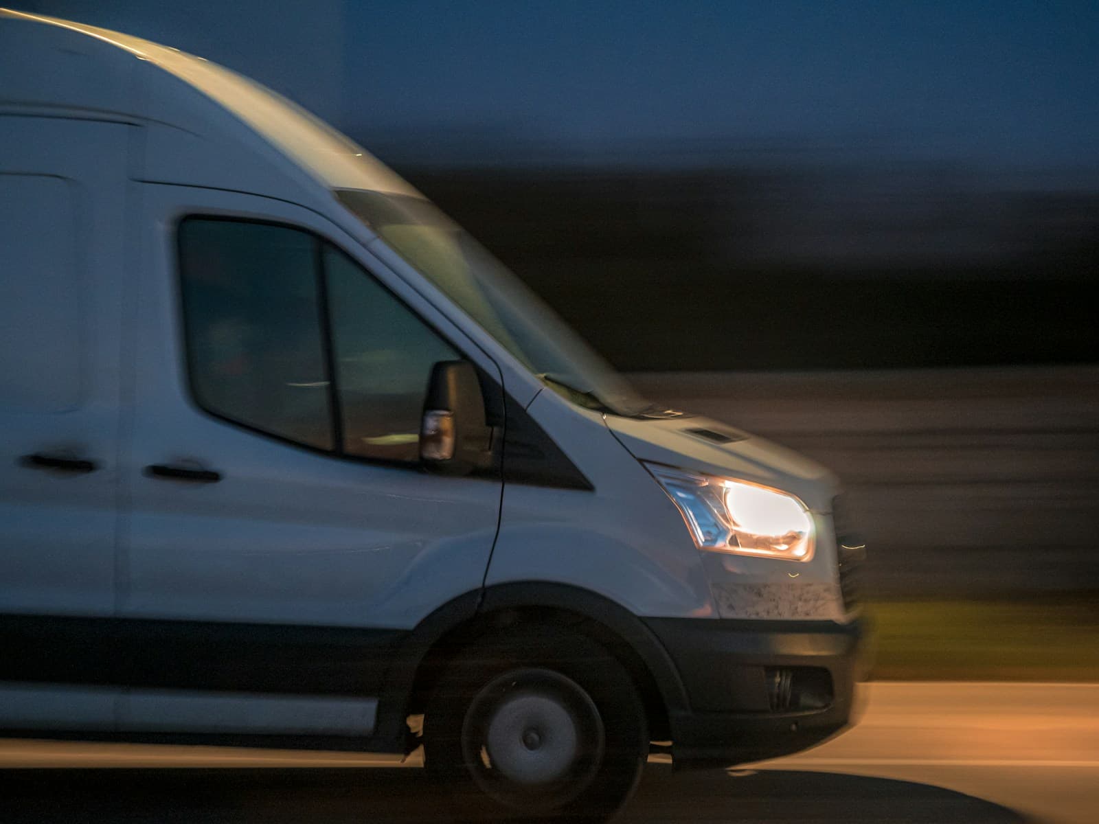 A cargo van at speed at night with its headlights on